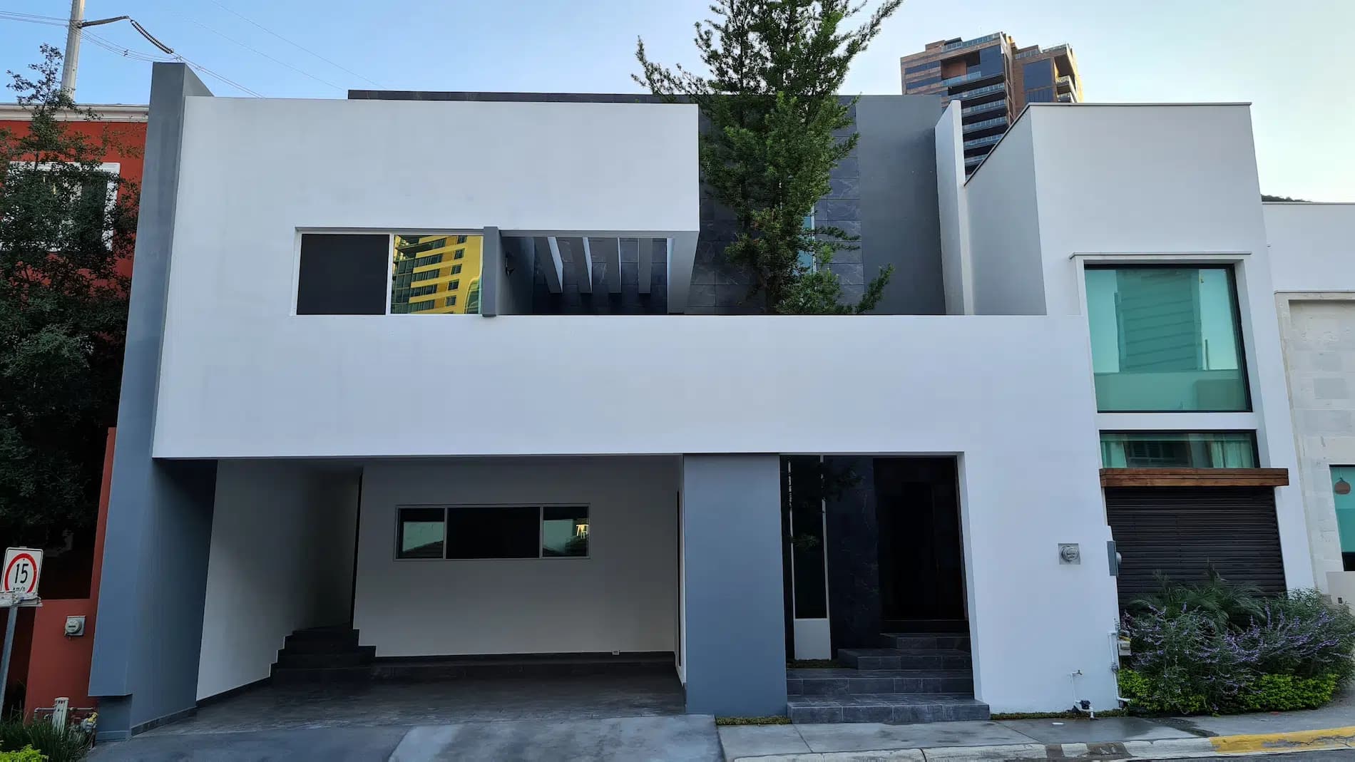Fachada blanca de casa moderna de dos niveles con cochera abierta y acceso en negro