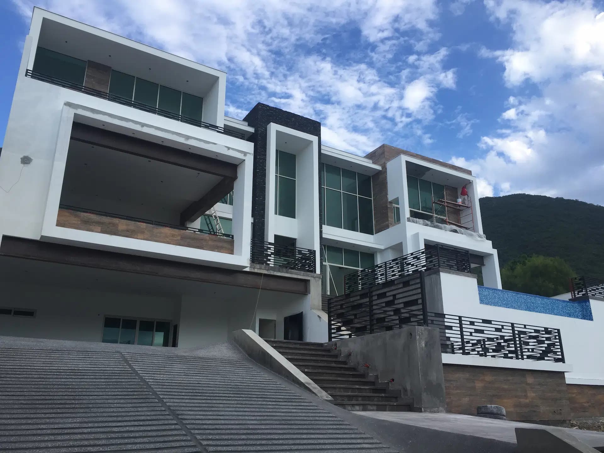 Residencia moderna blanca de varios volúmenes con terrazas, escalera y cerro al fondo