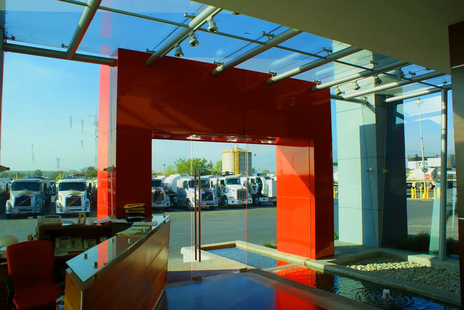 Recepción con pórtico rojo, escritorio de madera y patio de tractocamiones al fondo