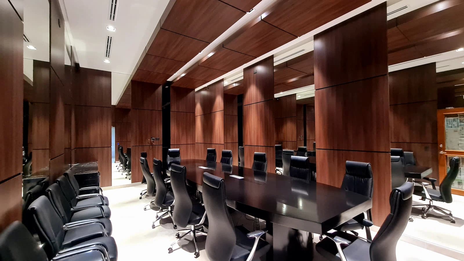 Sala de consejo con paneles de madera oscura, mesa negra larga y sillas de piel